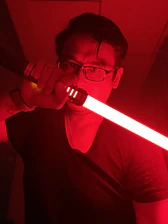 Close-up of a handcrafted lightsaber hilt glowing softly against a deep black background, highlighting fine metalwork and intricate details.