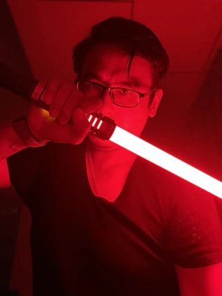 Close-up of a handcrafted lightsaber hilt glowing softly against a deep black background, highlighting fine metalwork and intricate details.