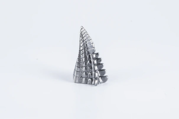 Minimalist presentation of a small sculptural object made of mixed metals displayed on a reflective black marble slab.