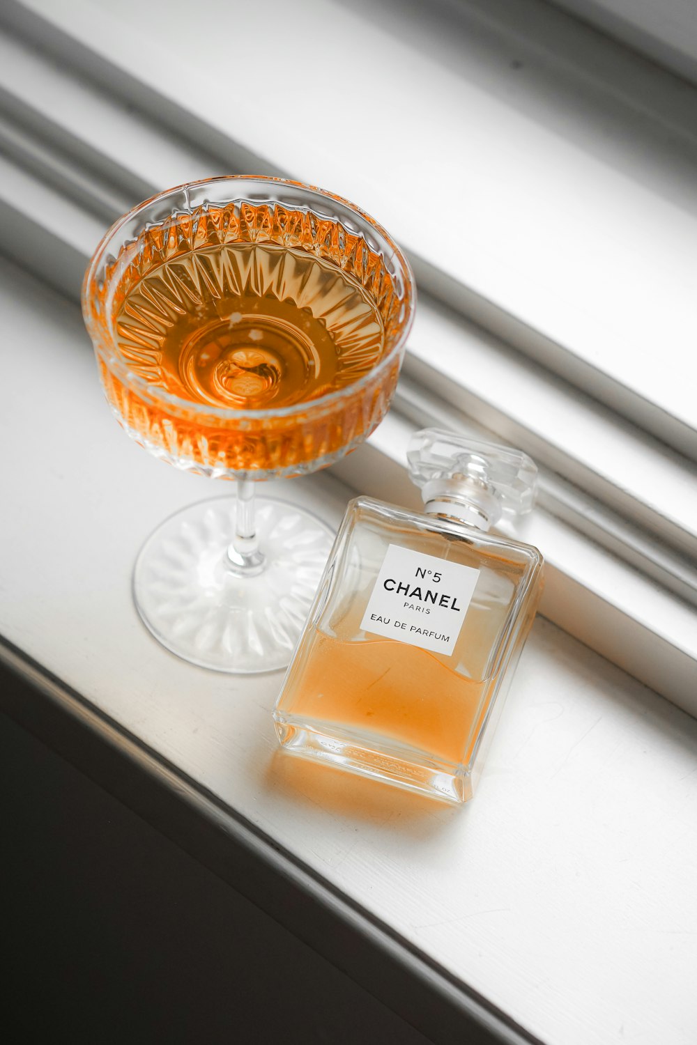 a bottle of chanel next to a glass on a window sill