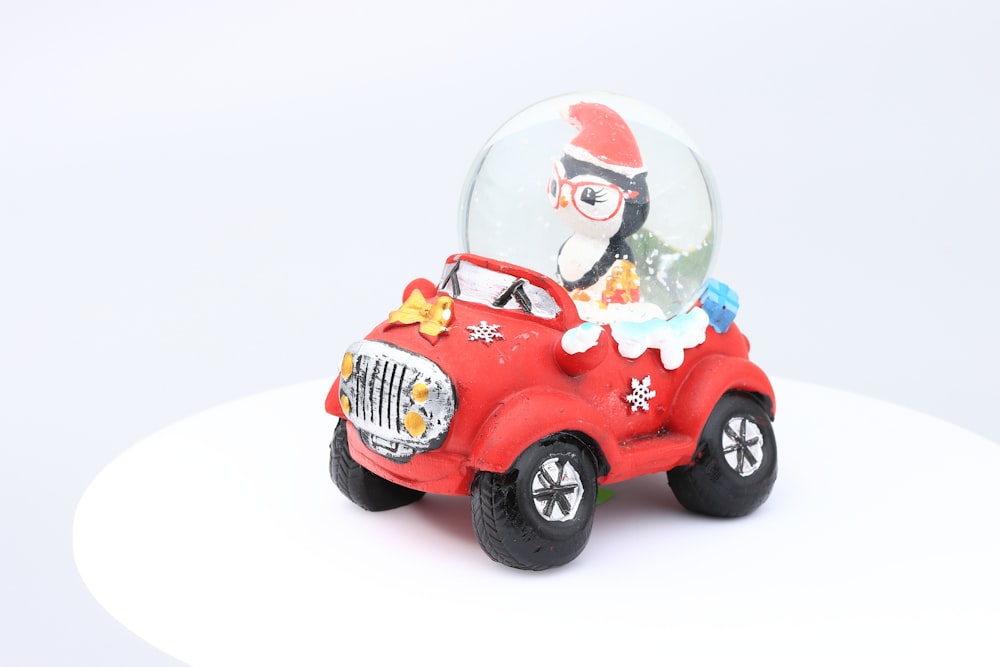 a red toy car with a snow globe on top of it