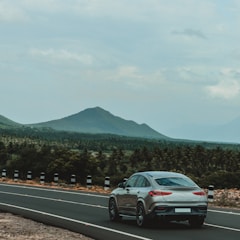 A sleek car driving through a scenic regional road with a happy passenger inside.