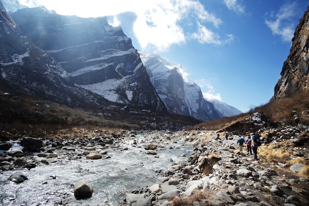 a group of people walking across a rocky river