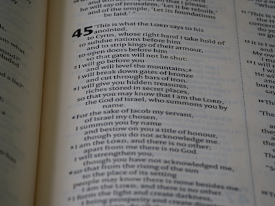 A close-up view of a book page showing text. The page contains a passage from a religious scripture, with verse numbers and text aligned in a structured format. The text is clearly printed in black ink on a light-colored background.