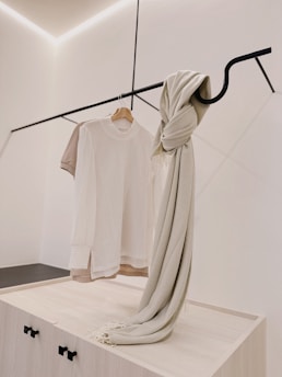 Minimalist clothing displayed on wooden hangers against a white wall.