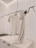 A minimalist clothing display with a white t-shirt on a wooden hanger and a beige knit scarf draped over a sleek black metal rod. The background is a clean, light-colored wall with subtle architectural lines.