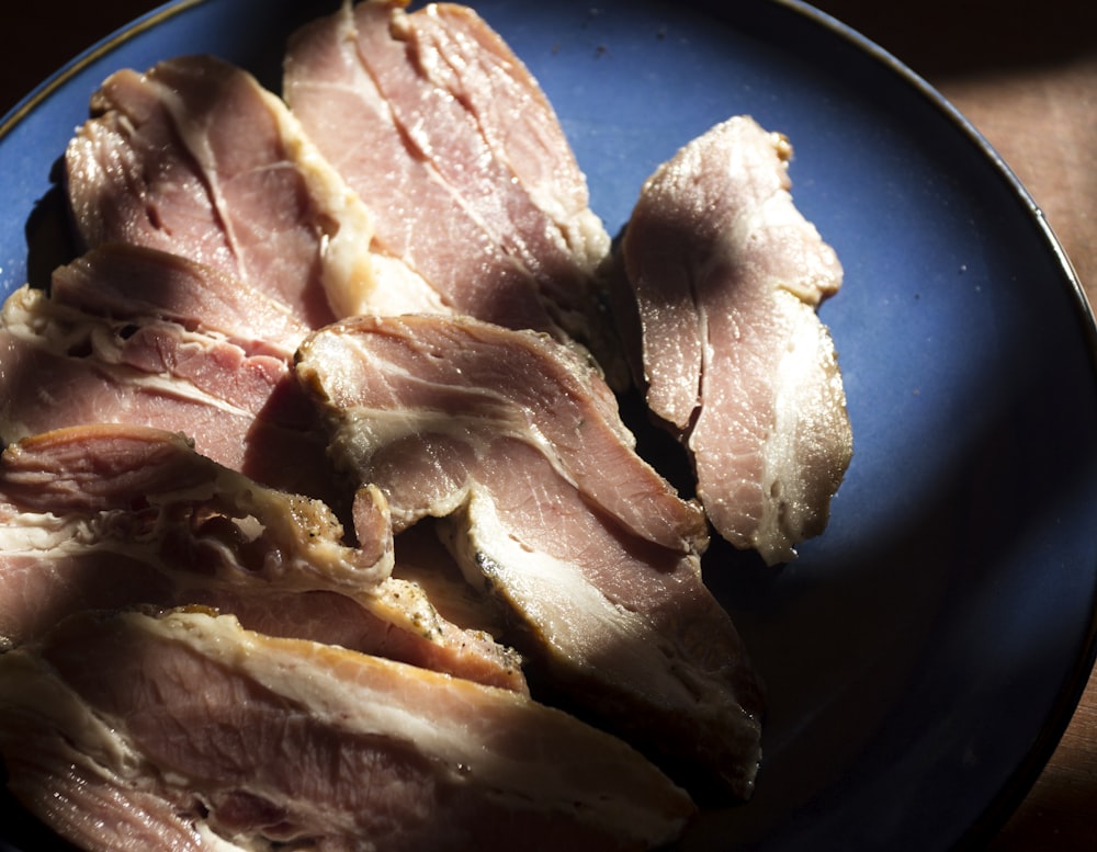a blue plate topped with sliced ham on top of a wooden table