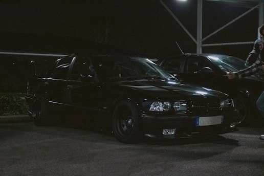 A close-up photo of a suspicious figure lurking near a parked car at dusk.