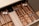 A neatly organized wooden cutlery drawer contains various types of utensils, including stainless steel and black-handled knives, forks, and spoons. Cloth napkins are folded and stored in one section, with silver and copper-toned utensils placed separately.