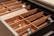 An organized kitchen drawer contains various utensils neatly arranged in wooden dividers. The utensils include spoons, forks, knives, and napkins. The dividers provide separate compartments for each type of cutlery, enhancing the aesthetic of the drawer's organization.