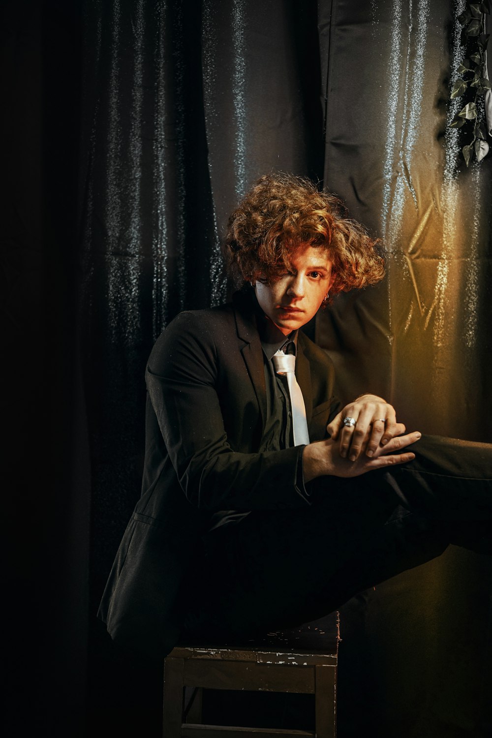 a man with curly hair sitting on a stool