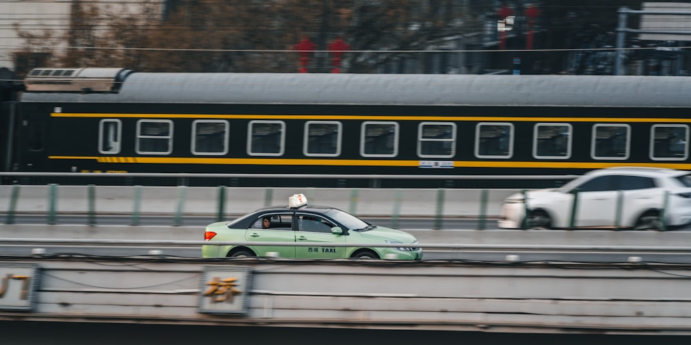 a green car driving down a street next to a train