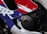 Close-up view of a motorcycle fairing with a vibrant design featuring red, blue, and white colors. The word 'Honda' is engraved on a circular, metallic engine cover. The area includes bolts and part of the chassis, highlighting motorcycle components and branding.