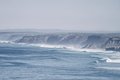 A ship sailing past a rugged coastline with waves gently crashing.