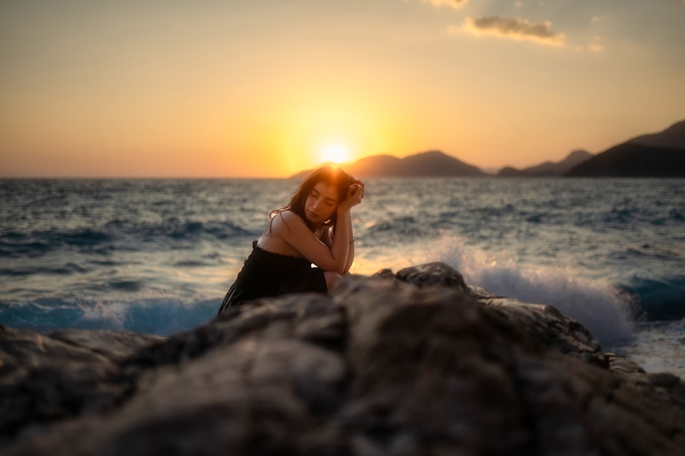 a woman sitting on a rock next to the ocean