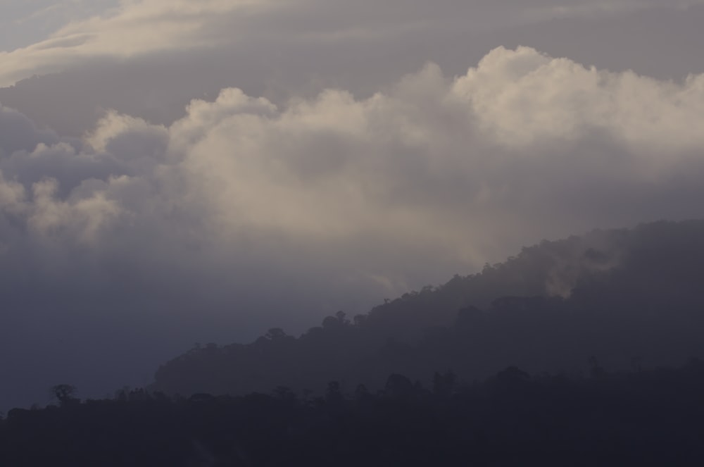 a plane flying through a cloudy sky with a mountain in the background