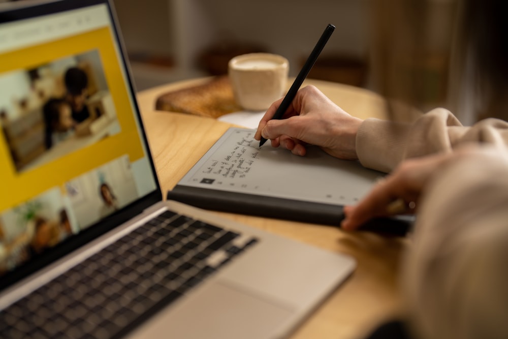 a person writing on a laptop with a pen