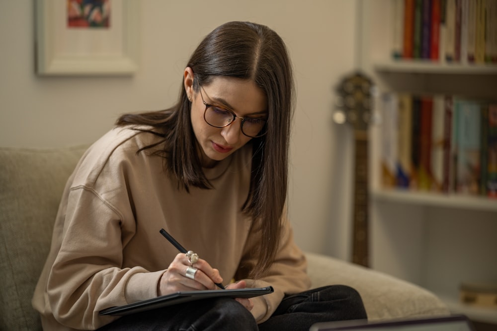 a woman sitting on a couch writing on a piece of paper