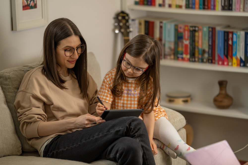 a woman and a girl sitting on a couch looking at a tablet