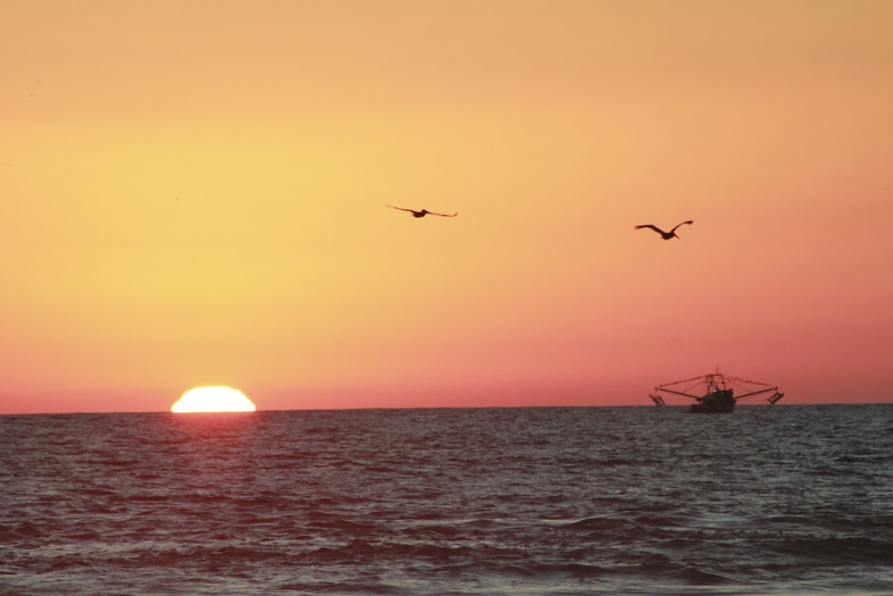 the sun is setting over the ocean with a boat in the water