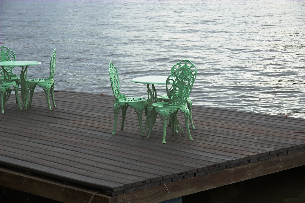 three green chairs and a table on a dock