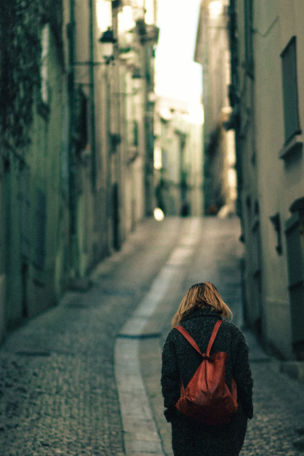 a woman walking down a street with a red backpack