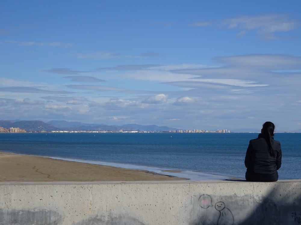 a person sitting on a concrete wall looking out at the ocean