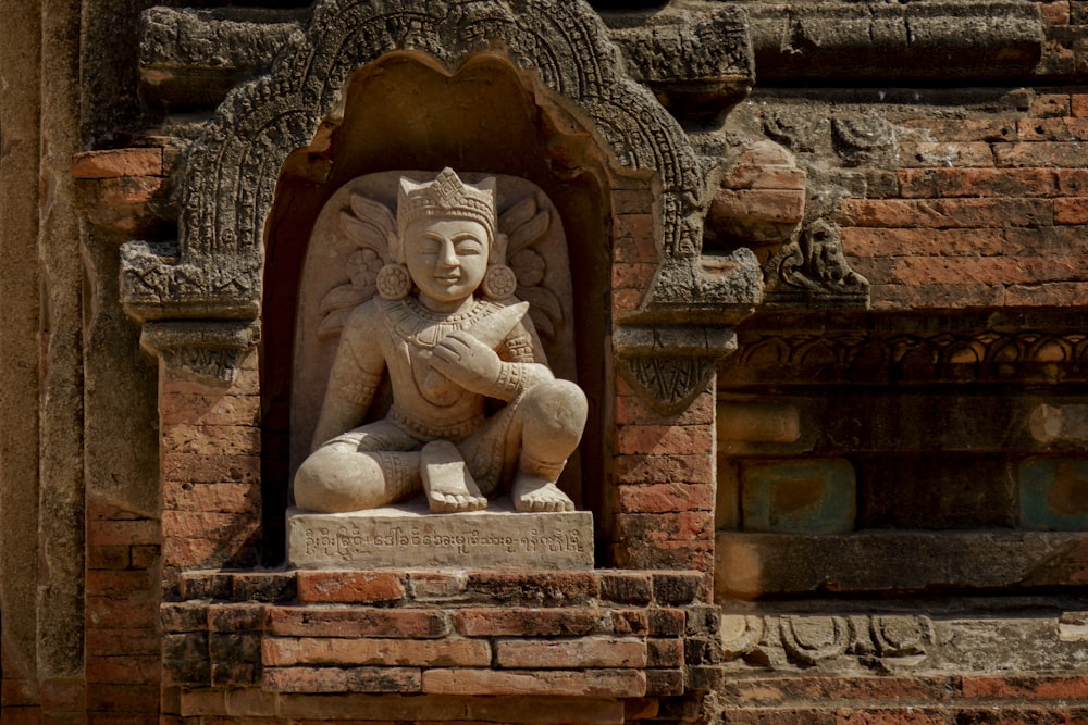 a statue of a person sitting on a brick wall