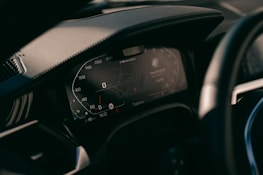 A close-up view of a car's digital dashboard display, showing various informational panels including a speedometer and GPS navigation system. The dashboard is modern with illuminated numbers and sleek design.