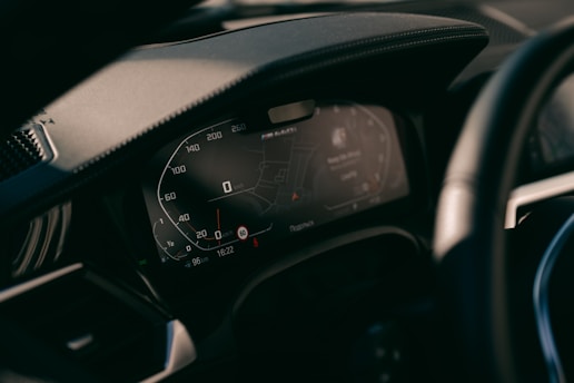 A close-up view of a car's digital dashboard display, showing various informational panels including a speedometer and GPS navigation system. The dashboard is modern with illuminated numbers and sleek design.