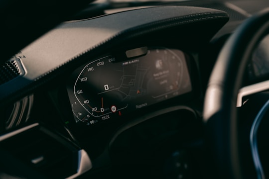 A close-up view of a car's digital dashboard display, showing various informational panels including a speedometer and GPS navigation system. The dashboard is modern with illuminated numbers and sleek design.