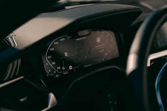 A close-up view of a car's digital dashboard display, showing various informational panels including a speedometer and GPS navigation system. The dashboard is modern with illuminated numbers and sleek design.