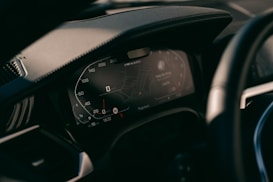 A close-up view of a car's digital dashboard display, showing various informational panels including a speedometer and GPS navigation system. The dashboard is modern with illuminated numbers and sleek design.