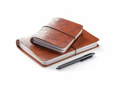 An assortment of elegant notebooks and journals stacked with a vintage pen resting on top.