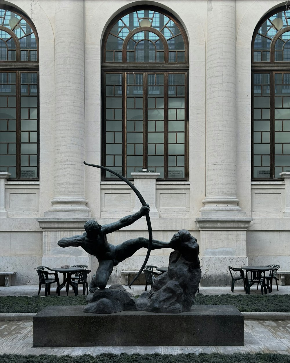 Una estatua de un hombre sosteniendo un arco y una flecha frente a un edificio