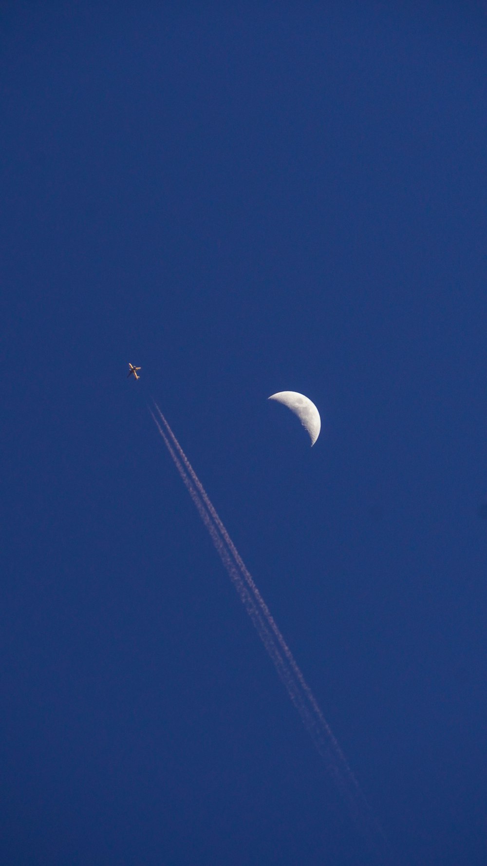 a plane flying in the sky with a half moon in the background