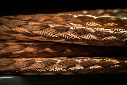 Close-up view of intricately braided copper wires with a shiny, metallic finish. The weaving pattern is detailed and reflects light, creating a warm, golden appearance.