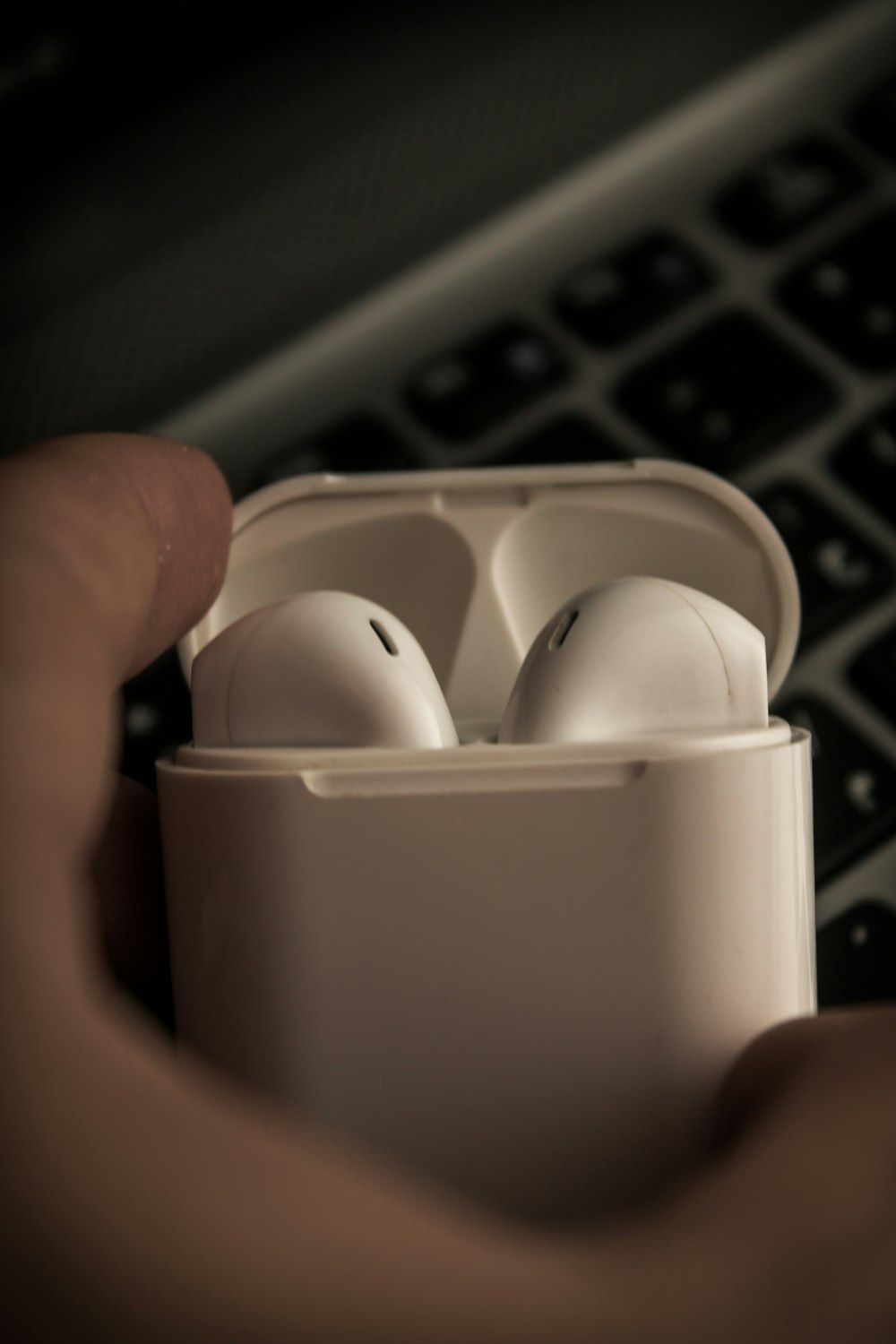 a person holding a pair of white earbuds in front of a keyboard