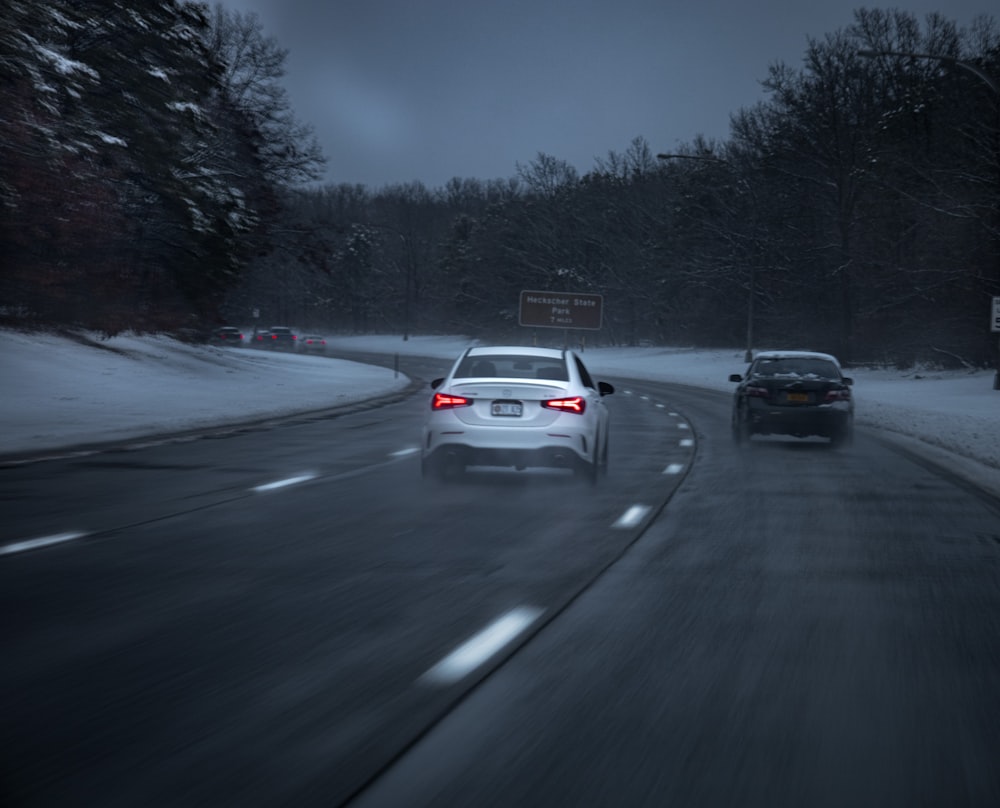 a couple of cars driving down a snow covered road