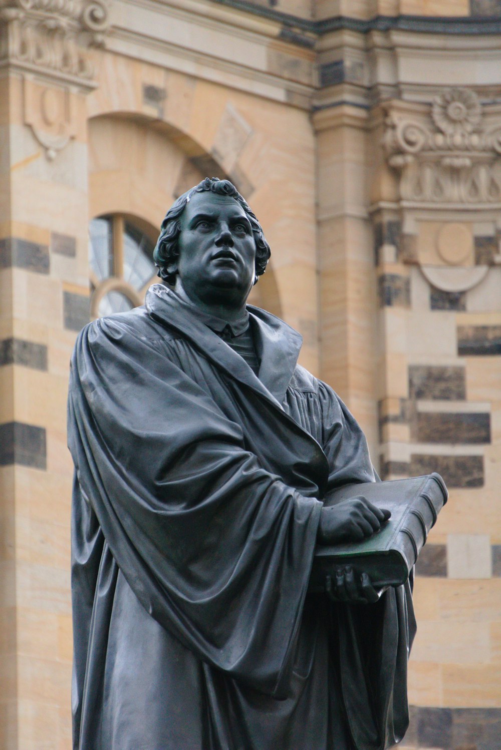 a statue of a man holding a book in front of a building