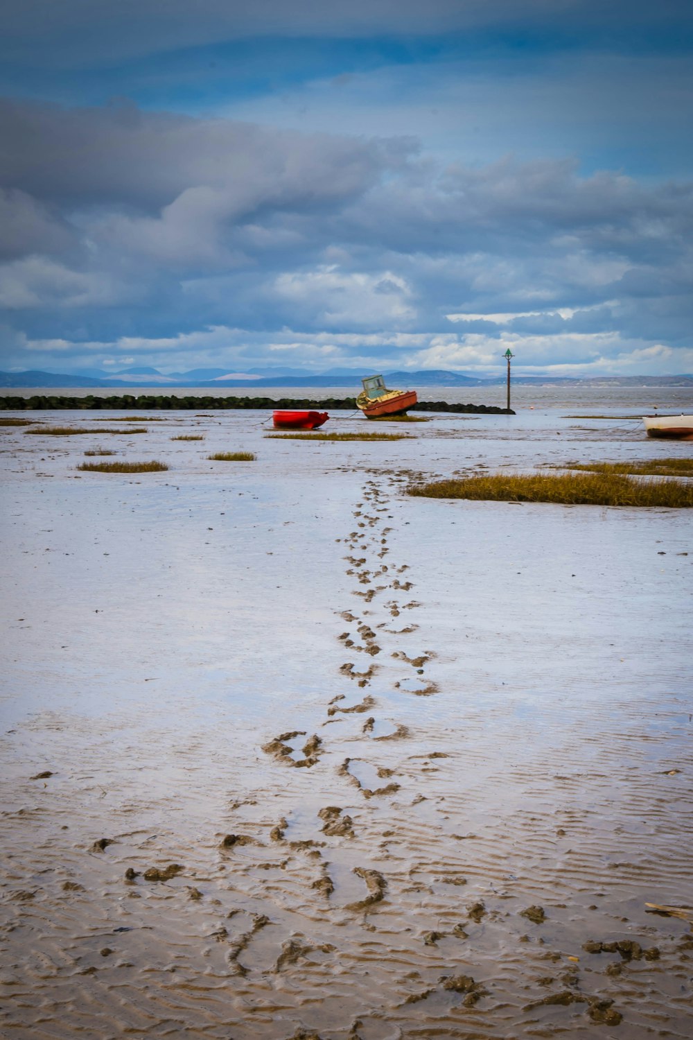 a beach with a boat and footprints in the sand