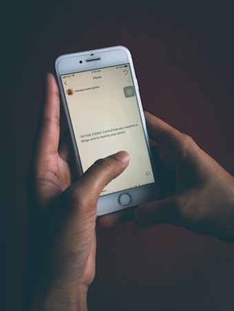 A person is holding a smartphone with both hands. The phone screen displays a message that reads, 'TIP FOR TODAY: Control how you respond to things sent to destroy your peace.' The background is dark, contrasting with the illuminated phone screen.