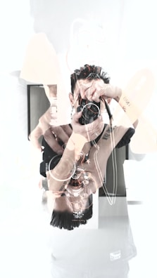 A double exposure effect with a person holding a camera, resulting in a visually layered and abstract appearance. Intricate tattoo art is visible on the arm, set against a bright, high-contrast background.