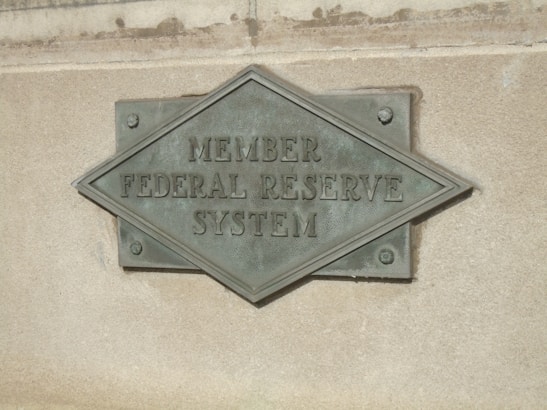 A textured metal plaque mounted on a stone surface, with the words 'Member Federal Reserve System' engraved in a diamond shape.