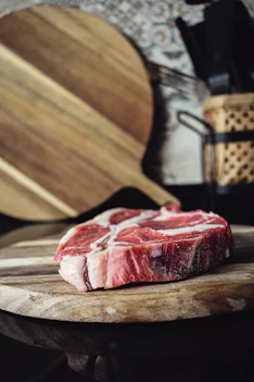Close-up of a thick, marbled ribeye steak resting on a wooden cutting board.
