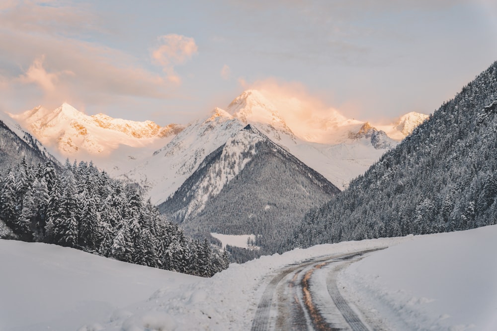 a snow covered road with mountains in the background