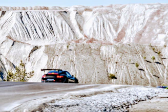 Side view of a matte gray car with a wide, aerodynamic spoiler on a winding mountain road.