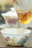 A hand pouring amber tea into a small porcelain cup, capturing the rich color.