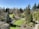 A beautifully landscaped garden featuring a variety of trees and bushes. The garden has a well-maintained lawn and a small pond. A winding stone path meanders through the greenery, with vibrant trees and neatly trimmed plants.