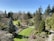 A beautifully landscaped garden featuring a variety of trees and bushes. The garden has a well-maintained lawn and a small pond. A winding stone path meanders through the greenery, with vibrant trees and neatly trimmed plants.